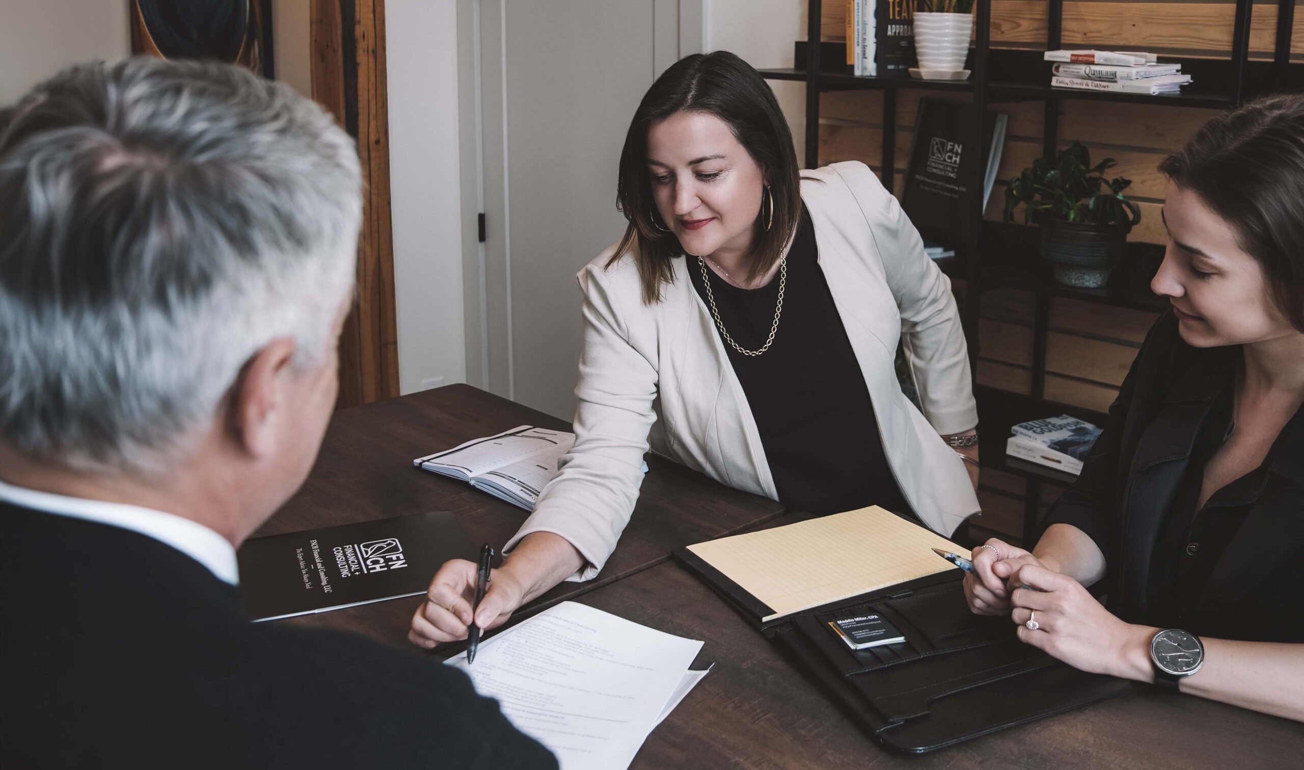 Two women signing financial documents with an older man in the foreground.