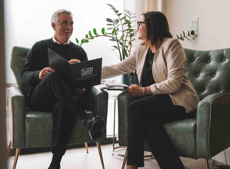 Business woman sits with business man between two seats in an office.